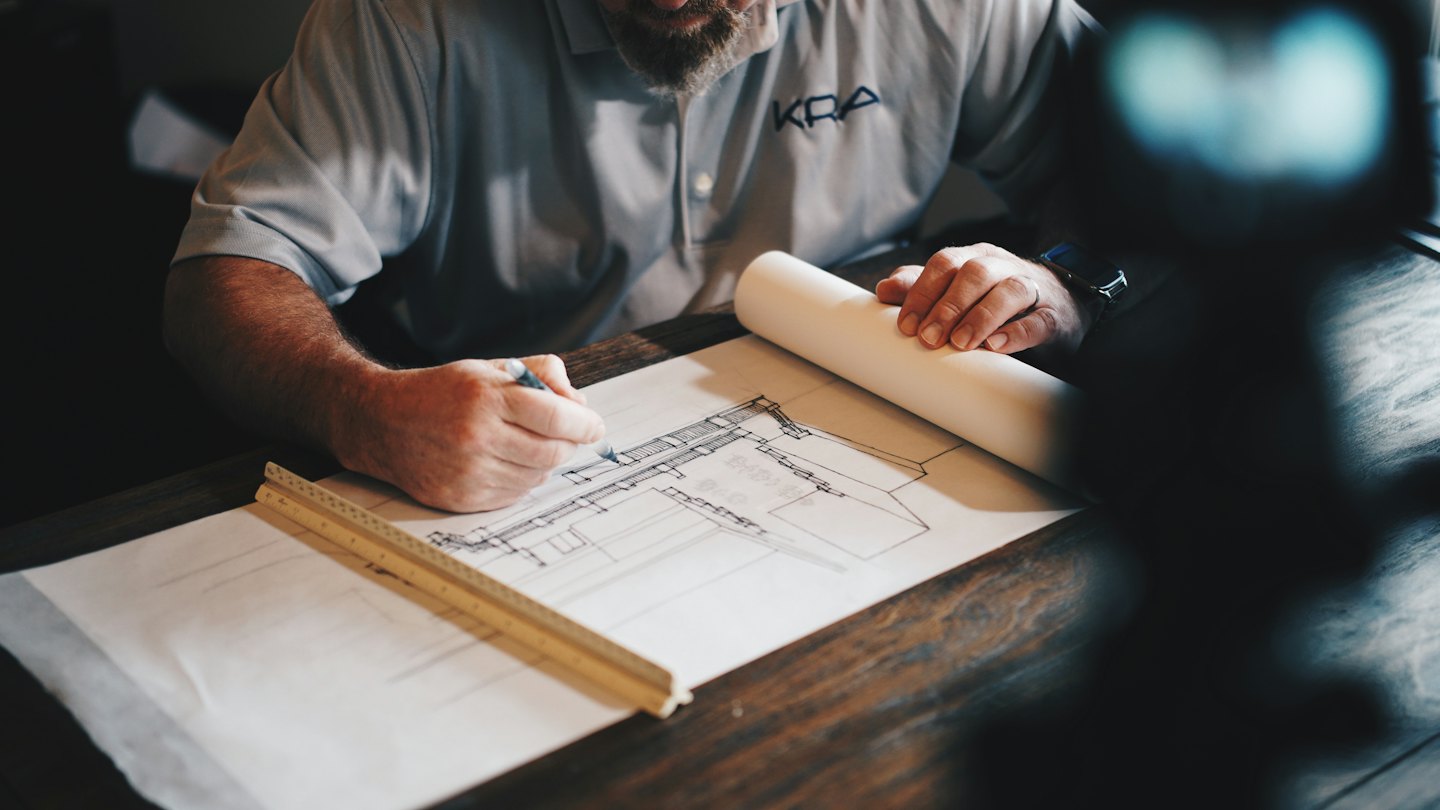 Professional sketching architectural plans on a wooden desk.