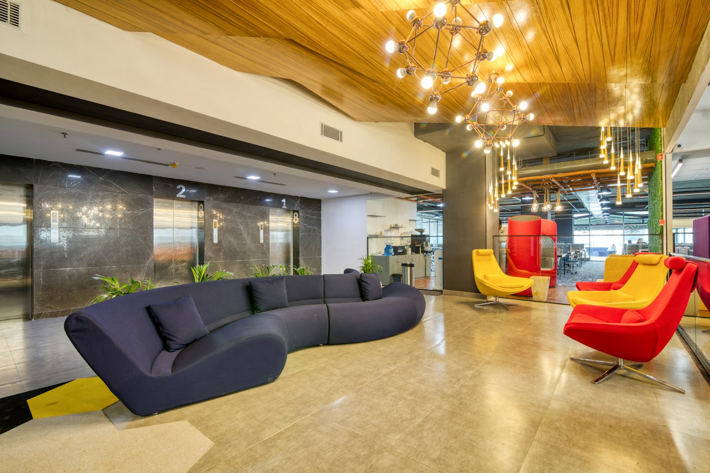 Modern office reception area with blue sofa and red chairs.